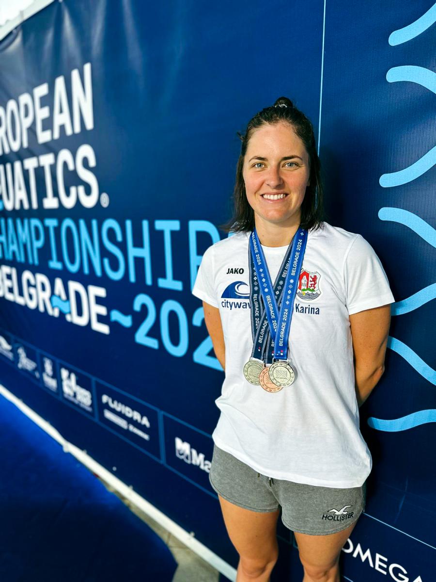 Karina Sommer, Expertin für Schwimmtrainingslager bei SOCCA GROUP, steht mit mehreren Medaillen vor dem Banner der European Aquatics Championships 2024 in Belgrad.
