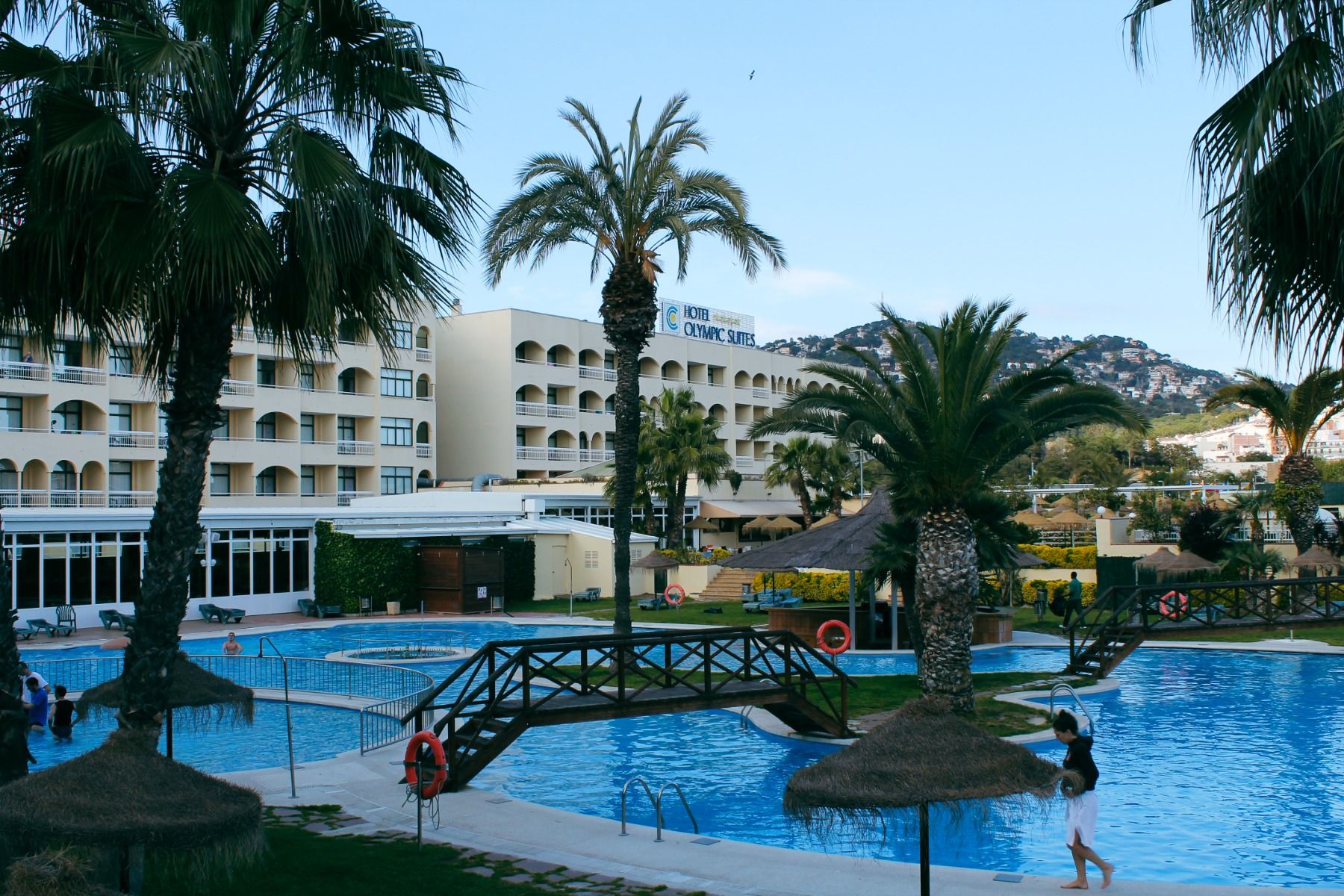 Hotelanlage mit Poollandschaft, Palmen, kleinen Brücken und Blick auf die umliegenden Berge.