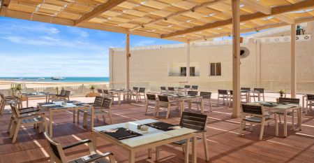 Aqua Vista Resort offers multiple outdoor pools, sun loungers, and umbrellas beneath clear blue skies—perfect for ein erfolgreiches Trainingslager in den Wintermonaten—with buildings and the sea in the background.