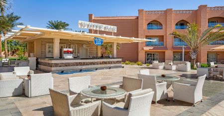 Aqua Vista Resort offers multiple outdoor pools, sun loungers, and umbrellas beneath clear blue skies—perfect for ein erfolgreiches Trainingslager in den Wintermonaten—with buildings and the sea in the background.