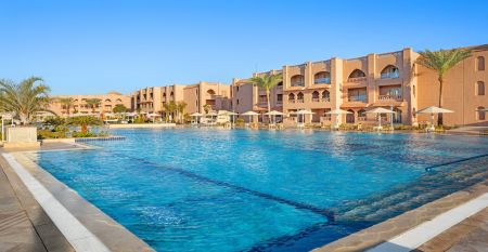 Aqua Vista Resort offers multiple outdoor pools, sun loungers, and umbrellas beneath clear blue skies—perfect for ein erfolgreiches Trainingslager in den Wintermonaten—with buildings and the sea in the background.