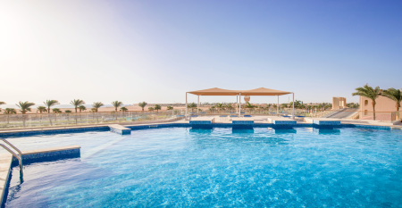 Aqua Vista Resort offers multiple outdoor pools, sun loungers, and umbrellas beneath clear blue skies—perfect for ein erfolgreiches Trainingslager in den Wintermonaten—with buildings and the sea in the background.
