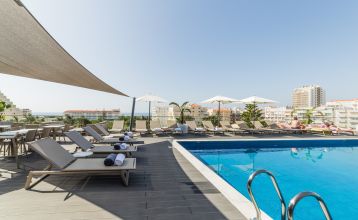 Außenansicht eines modernen Hotelgebäudes mit Balkonen und einem begrünten Vorgarten.