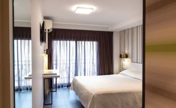 Das moderne New Hotel Colon mit mehreren Stockwerken, Balkonen und einer gepflegten Fassade, umgeben von grünen Bäumen und urbaner Architektur.