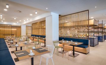 Modernes Hotelgebäude bei Nacht mit beleuchtetem Eingang und Kakteen im Vordergrund.
