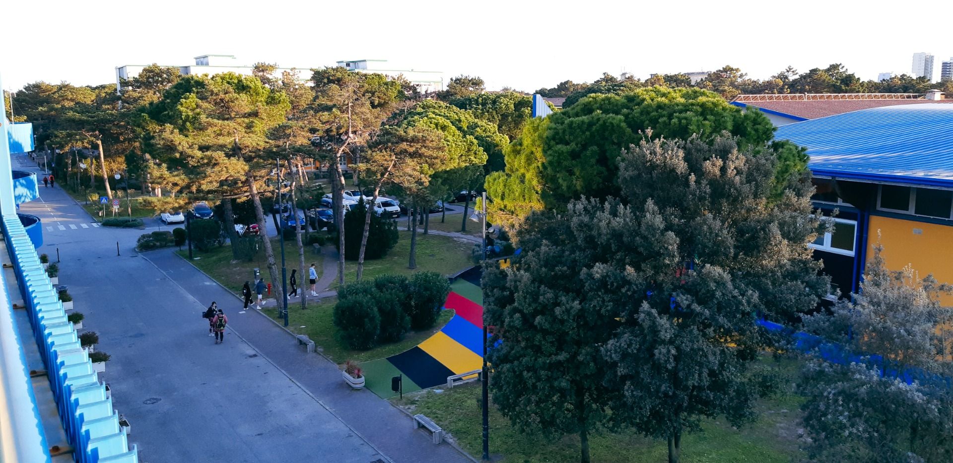 Blick auf das Bella Italia & EFA Village mit einer von Bäumen gesäumten Allee, bunten Gehwegen und moderner Architektur