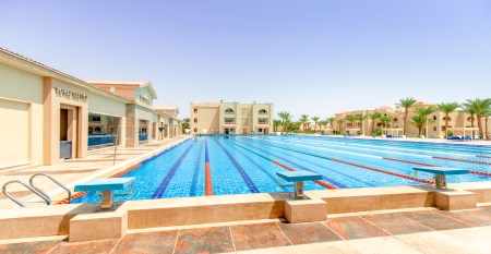 Aqua Vista Resort offers multiple outdoor pools, sun loungers, and umbrellas beneath clear blue skies—perfect for ein erfolgreiches Trainingslager in den Wintermonaten—with buildings and the sea in the background.