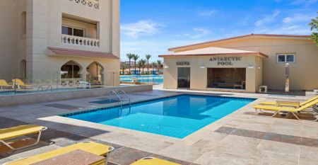 Aqua Vista Resort offers multiple outdoor pools, sun loungers, and umbrellas beneath clear blue skies—perfect for ein erfolgreiches Trainingslager in den Wintermonaten—with buildings and the sea in the background.