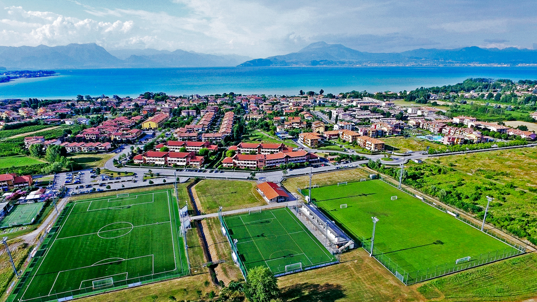 Fu&szlig;ballpl&auml;tze inmitten einer mediterranen Stadtlandschaft mit Blick auf einen blauen See und umliegende Berge.