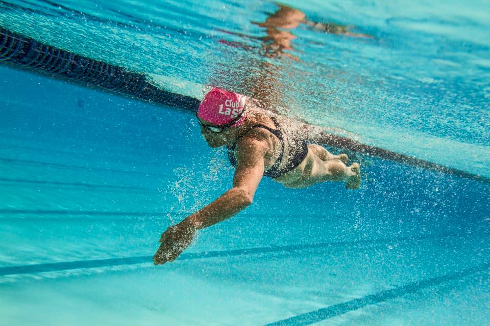 Unterwasseraufnahme einer Schwimmerin mit pinker Badekappe im Schwimmbecken, umgeben von Luftblasen.