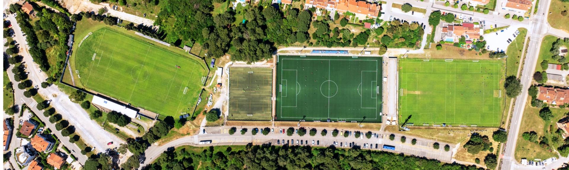 Fußballanlage aus der Vogelperspektive; zwei Rasenplätze und ein Kunstrasenplatz; mediterranes Flair