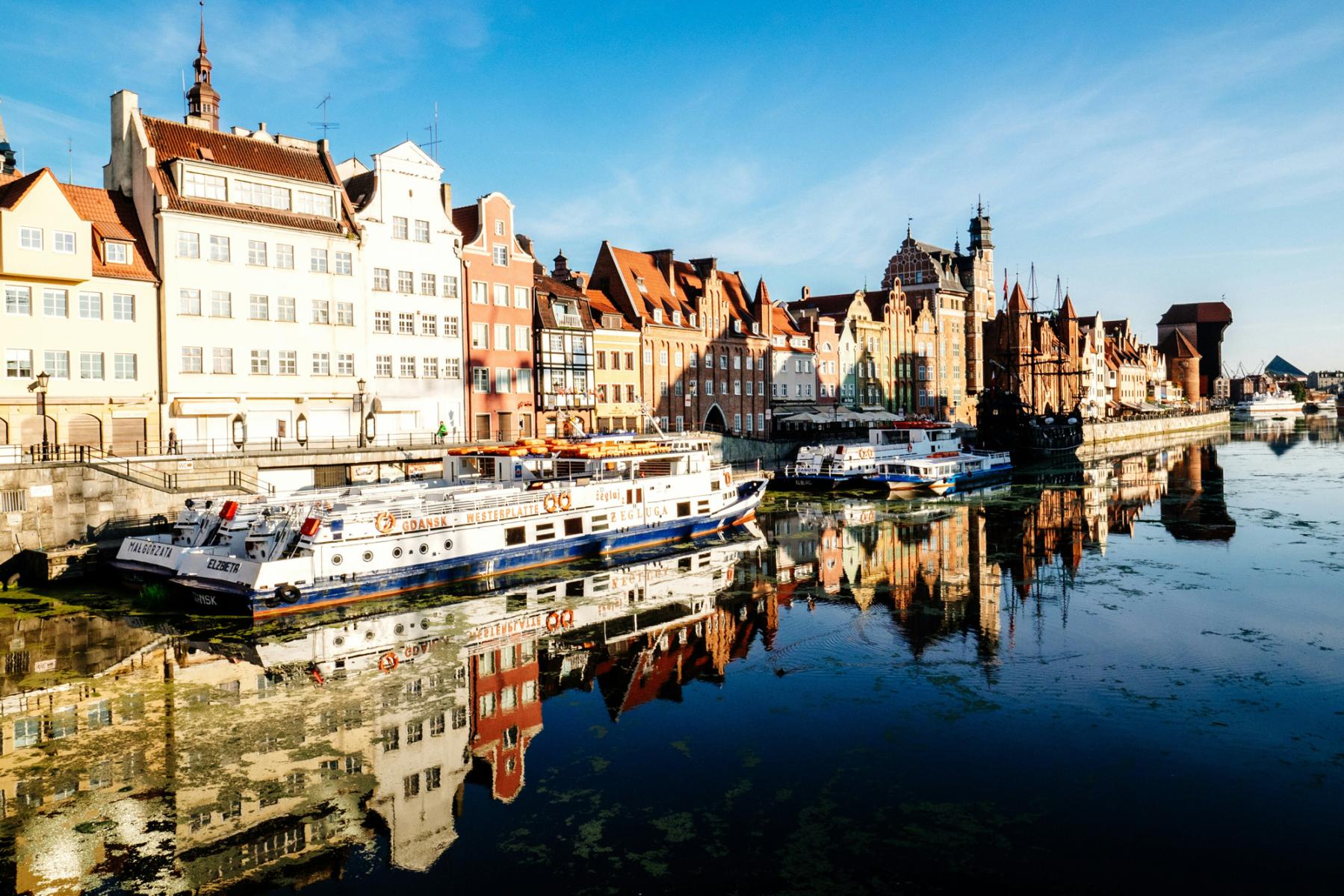 Historische Altstadt von Danzig, Polen, mit malerischen Fassaden entlang der Uferpromenade und Booten im Wasser bei sonnigem Wetter