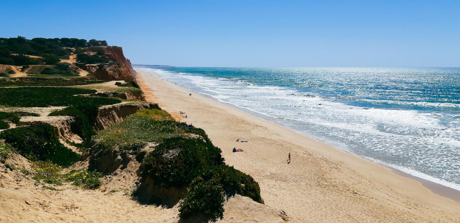 Atemberaubender Sandstrand in Portugal mit malerischen Klippen und klarem blauem Meer unter strahlend blauem Himmel