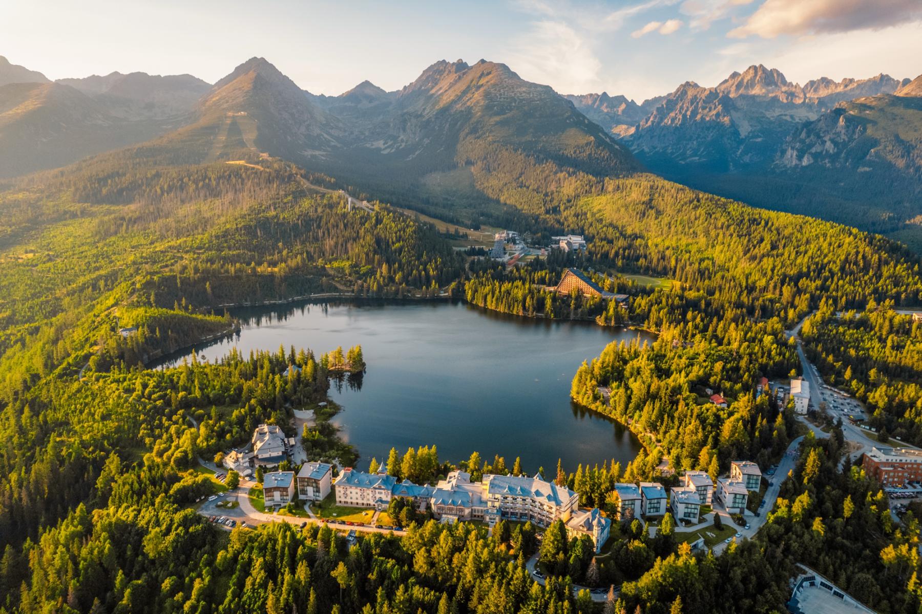 Malerischer Bergsee in der Slowakei, umgeben von dichten Wäldern und imposanten Bergen, mit Hotels und Gebäuden am Ufer in warmem Licht