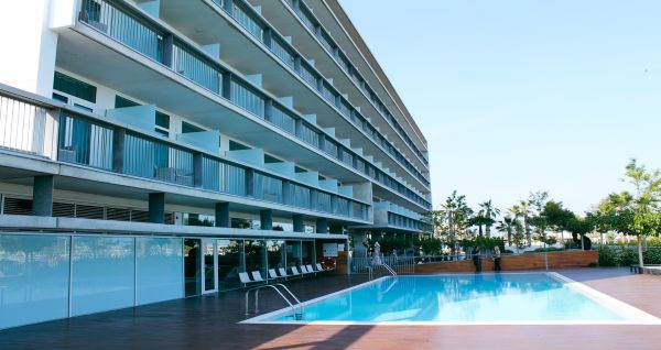 Außenansicht des Hotels mit Balkonen und einem großzügigen Poolbereich mit Liegestühlen und Holzboden.