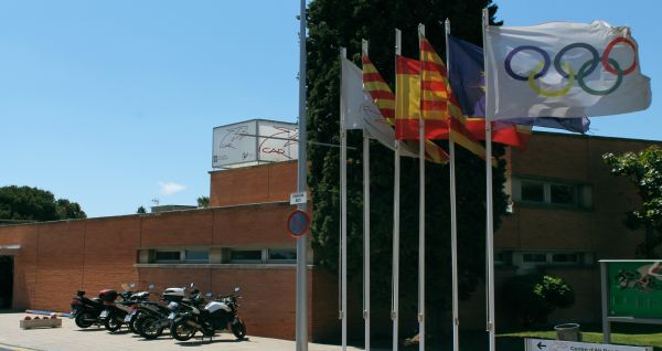 Eingang des CAR Centre d'Alt Rendiment mit wehenden Fahnen der Olympischen Spiele und regionalen Symbolen, daneben geparkte Motorräder.