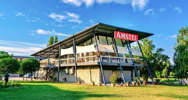Außenansicht des Hotels Amstel Hattyu Fogado mit moderner Architektur, großen Glasfronten und einer grünen Umgebung