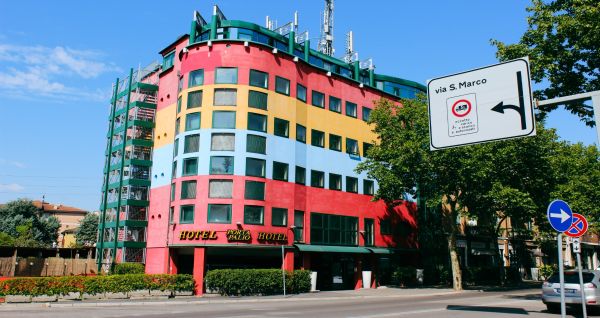 Außenansicht des Hotels Porta Palio mit auffälliger farbenfroher Fassade in Rot, Gelb und Blau, umgeben von Bäumen