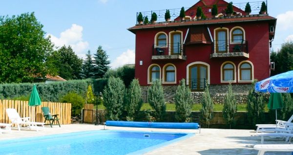 Rotes Hotelgebäude mit dekorativen Balkonen, einem Pool und gepflegter Gartenlandschaft.