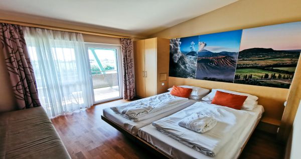 Ein helles Zimmer mit einem Doppelbett, orangen Kissen und einer großen Wanddekoration mit Naturmotiven.