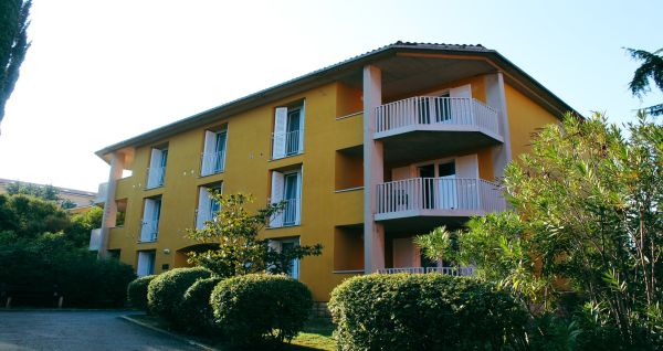 Außenansicht des gelben Gebäudes des Hotels San Simon Dependance, umgeben von Bäumen und Sträuchern.
