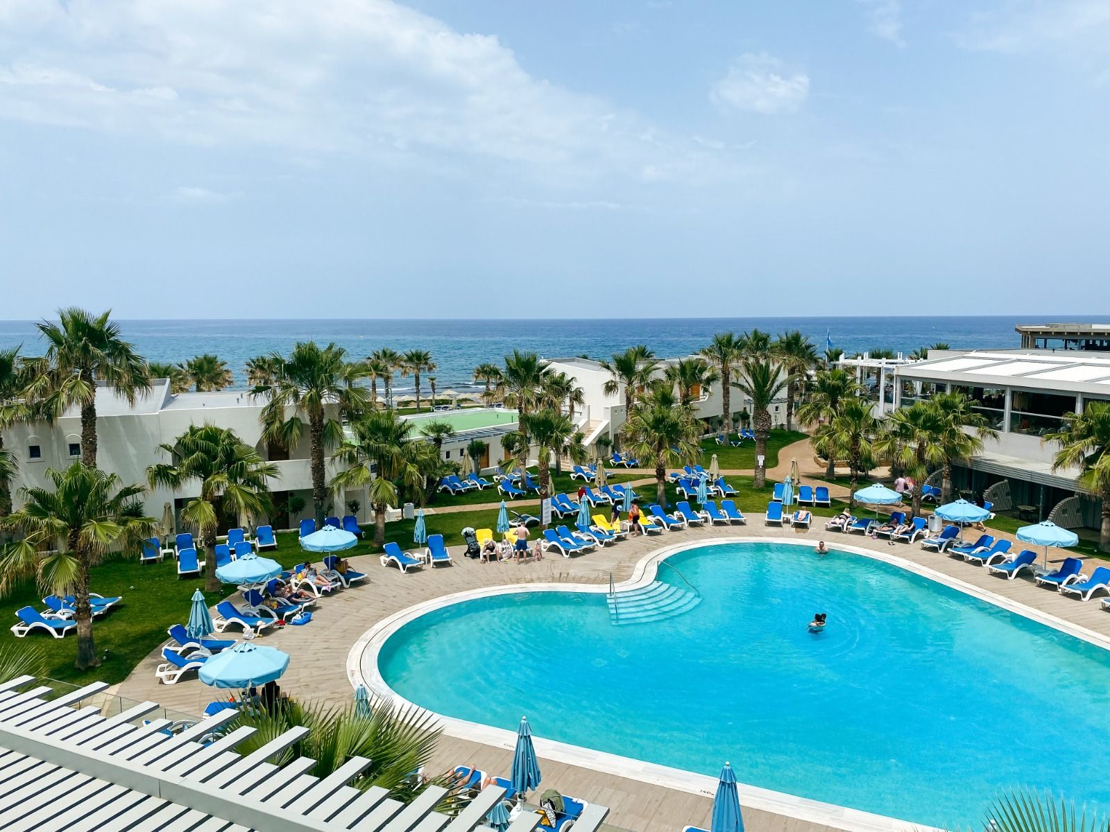 Blick auf einen weiteren Pool mit großem Liegebereich mit Palmen im Lyttos Beach Hotel, dahinter der Strand und das Meer 
