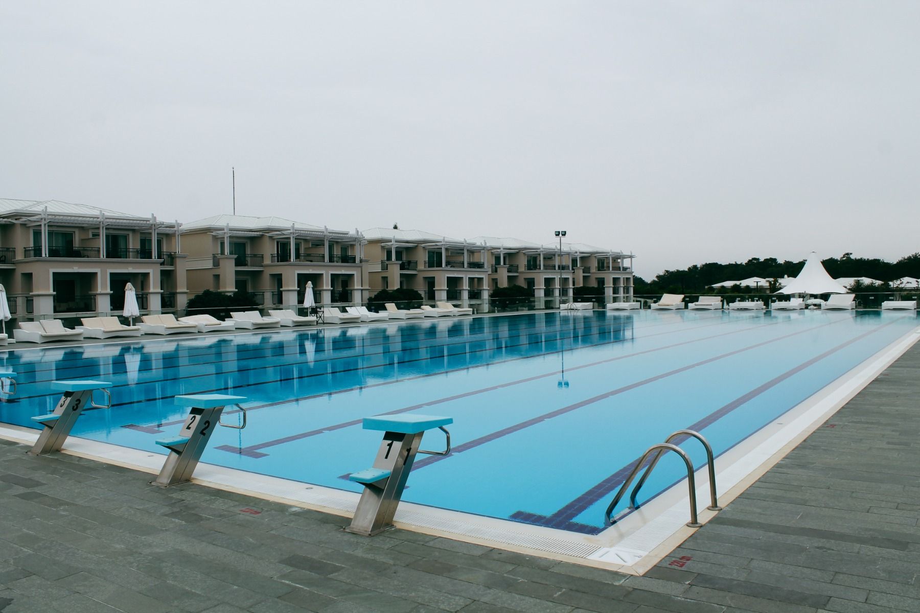 Olympisches Schwimmbecken, umgeben von komfortablen Villen und exklusiven Sonnenliegen.