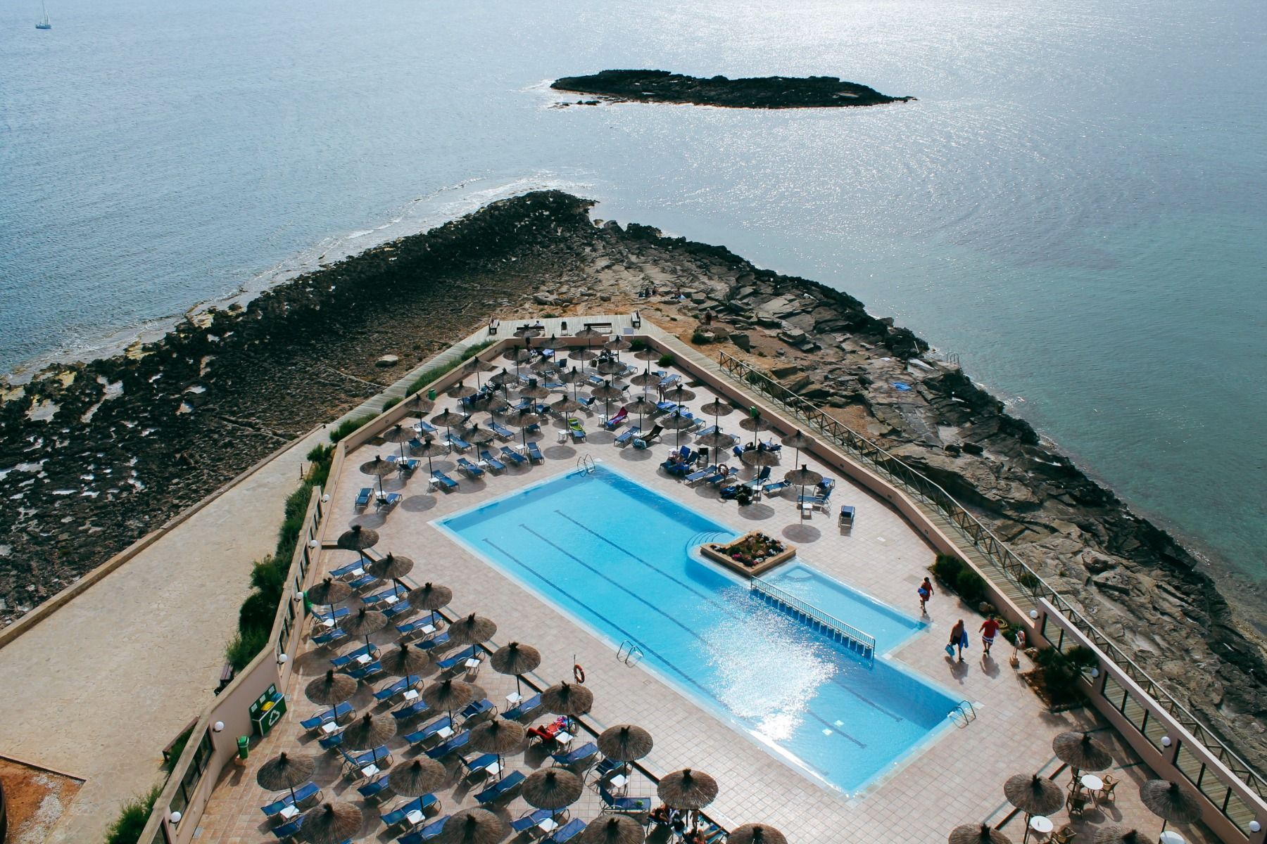 Ein beeindruckender Blick auf das Meer, mit einem Poolbereich im Vordergrund, ausgestattet mit Liegestühlen und Sonnenschirmen, direkt an der Küste gelegen.