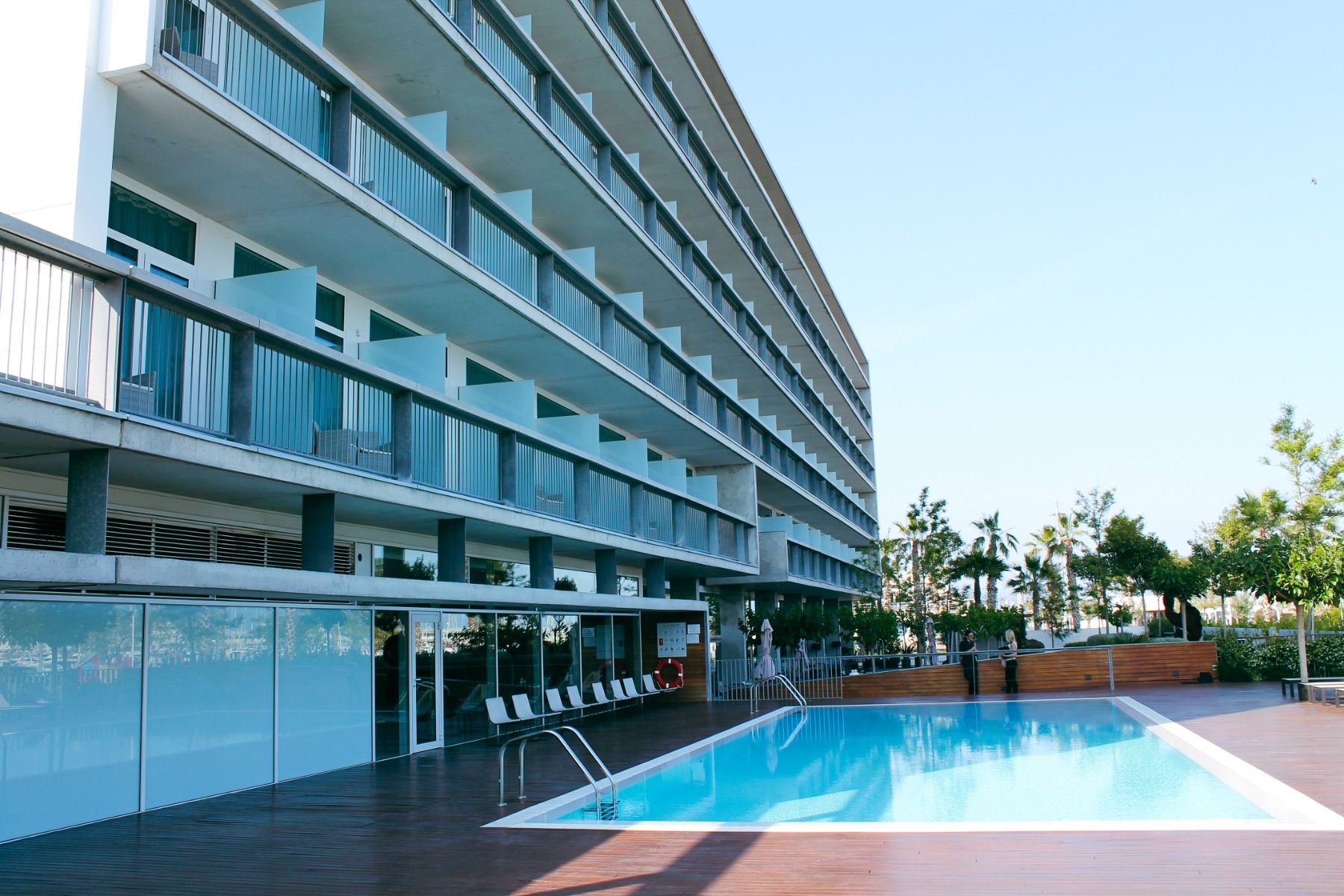 Außenansicht des Hotels mit Balkonen und einem großzügigen Poolbereich mit Liegestühlen und Holzboden.