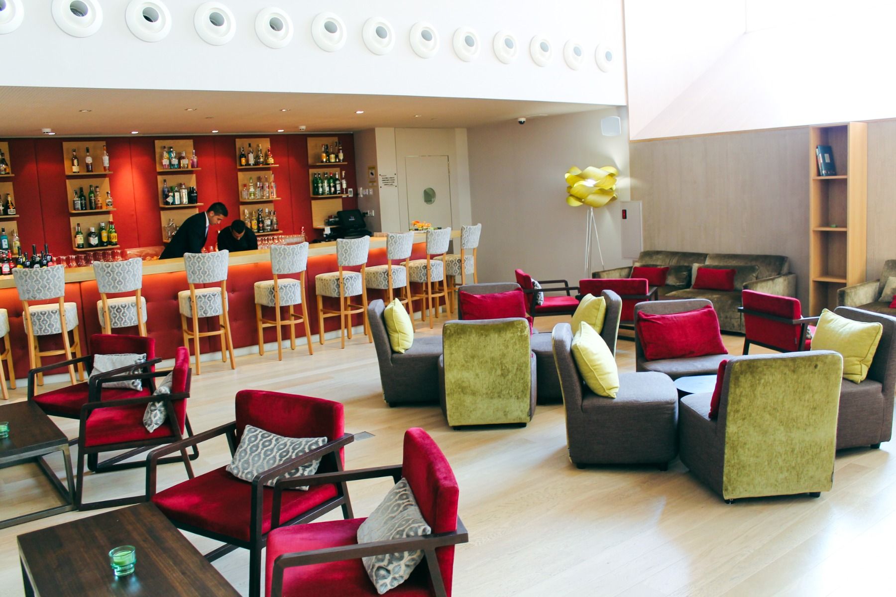 Elegante Hotelbar mit roten und grünen Sitzmöbeln, einer gut bestückten Theke und zwei Barkeepern.