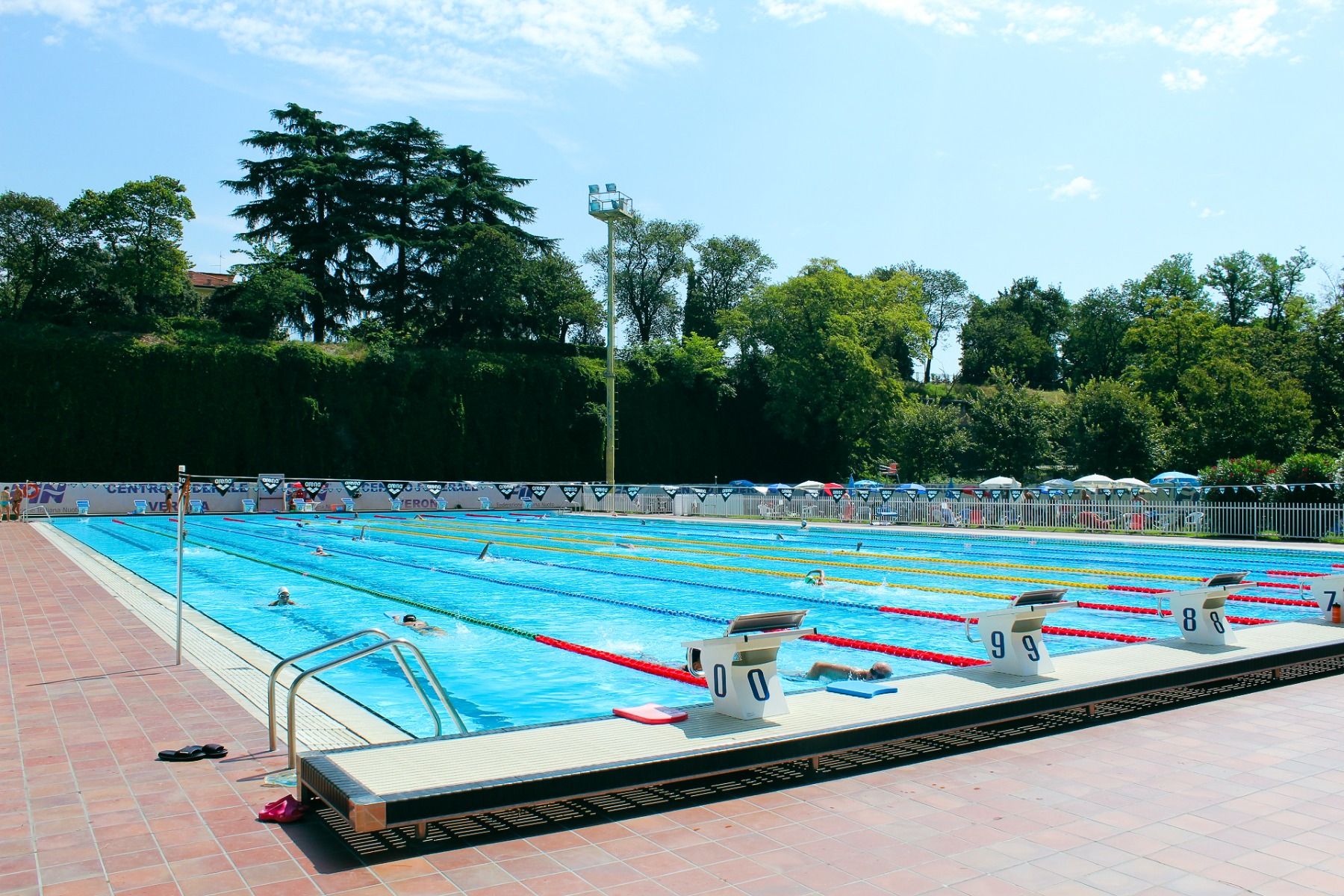 Großes, professionelles Freibad mit vielen Bahnen und insgesamt zehn Startblöcken, rundherum viel Grün und blauer Himmel