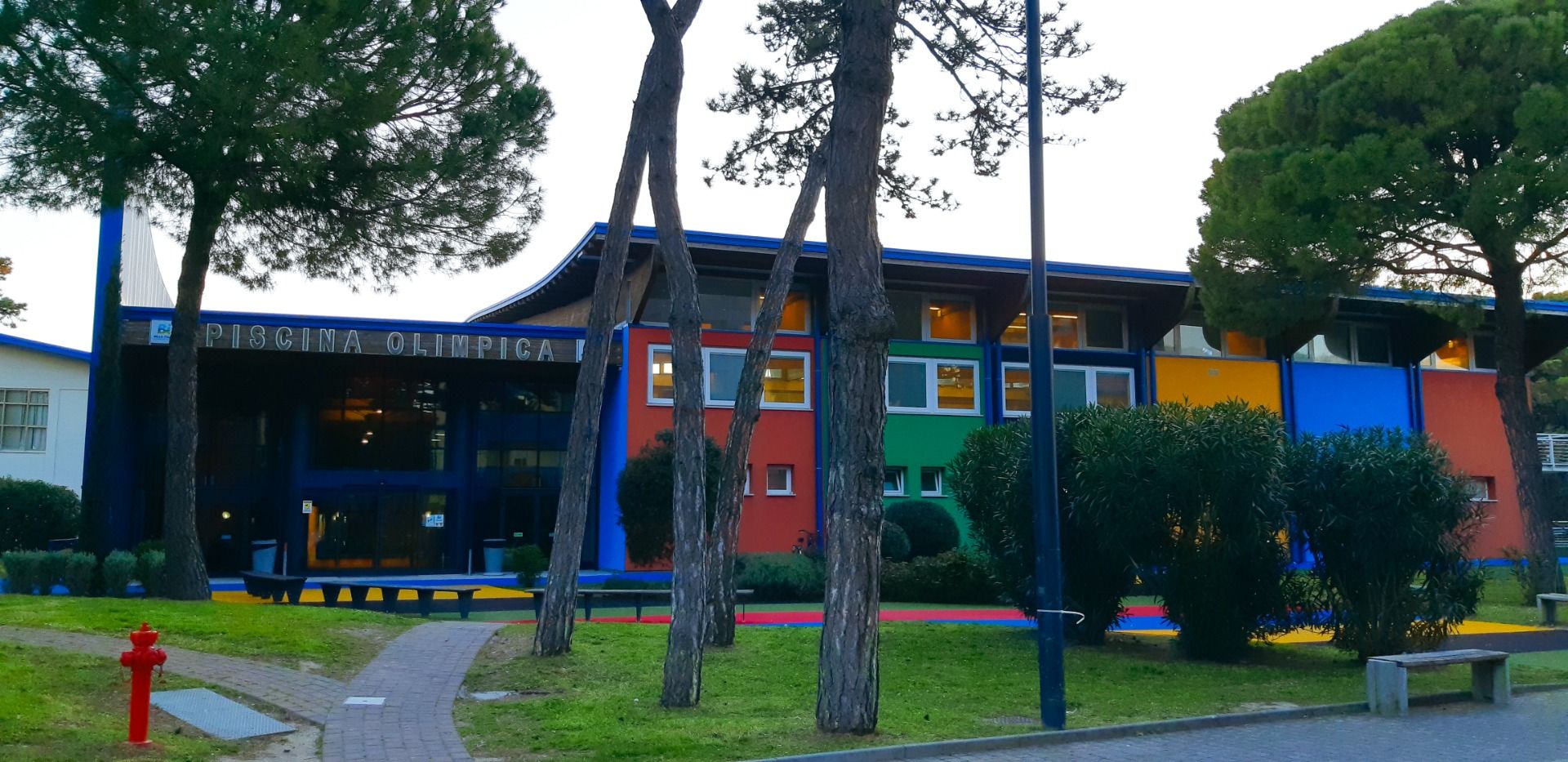 Bunte Fassade der Piscina Olimpica im Bella Italia & EFA Village, umgeben von Pinien und Grünflächen
