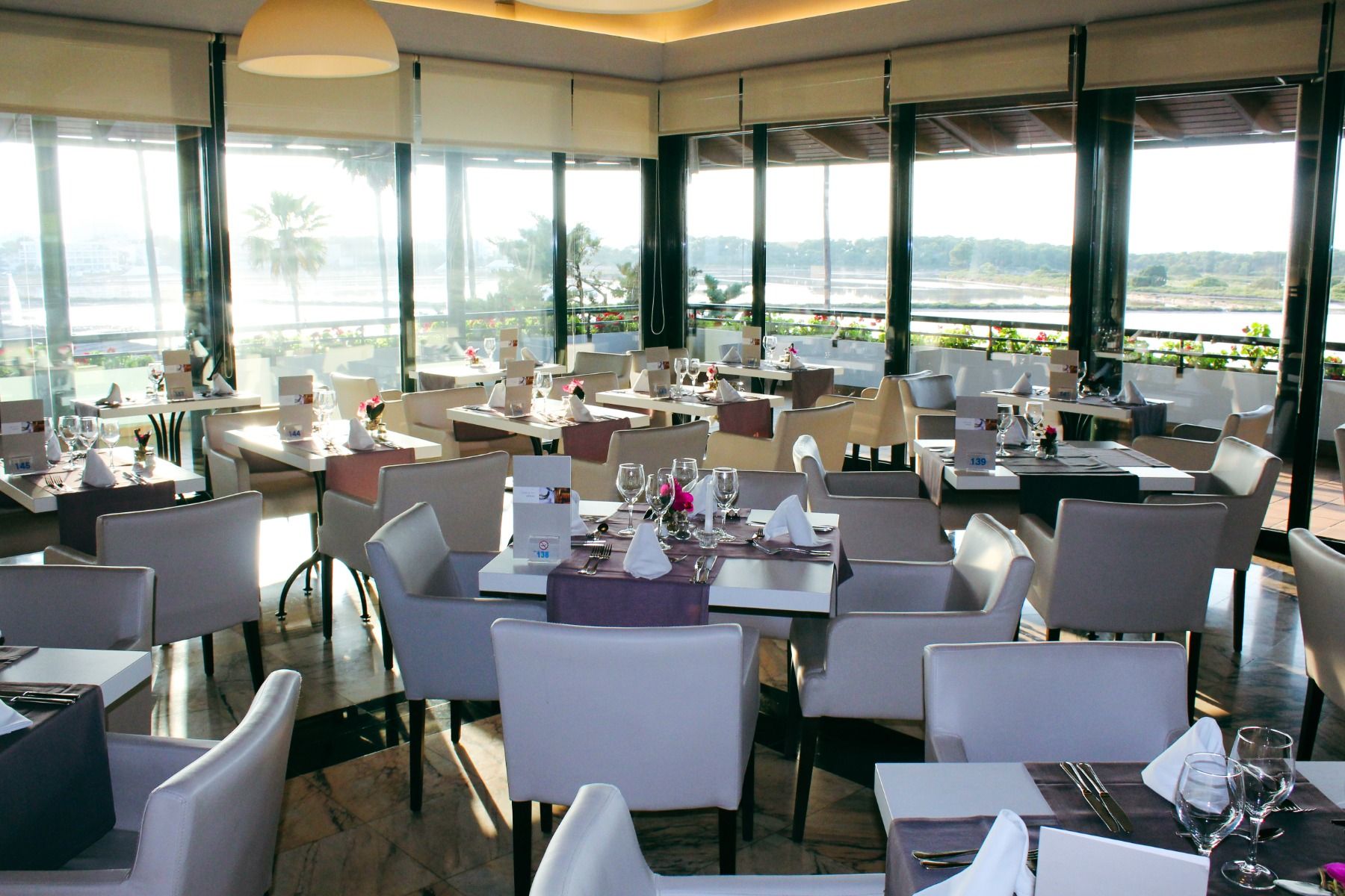 Modern eingerichtetes Restaurant des Blau Club mit gedeckten Tischen und Blick auf die Terrasse sowie die umliegende Landschaft.
