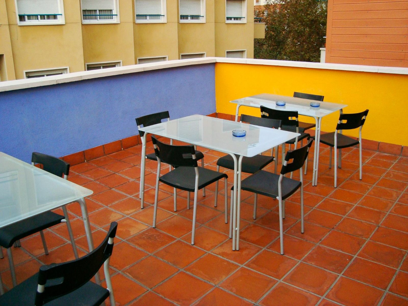Außenbereich des Hotels mit einer bunten Terrasse und Sitzgelegenheiten auf Terrakottafliesen, umgeben von mehrstöckigen Gebäuden.