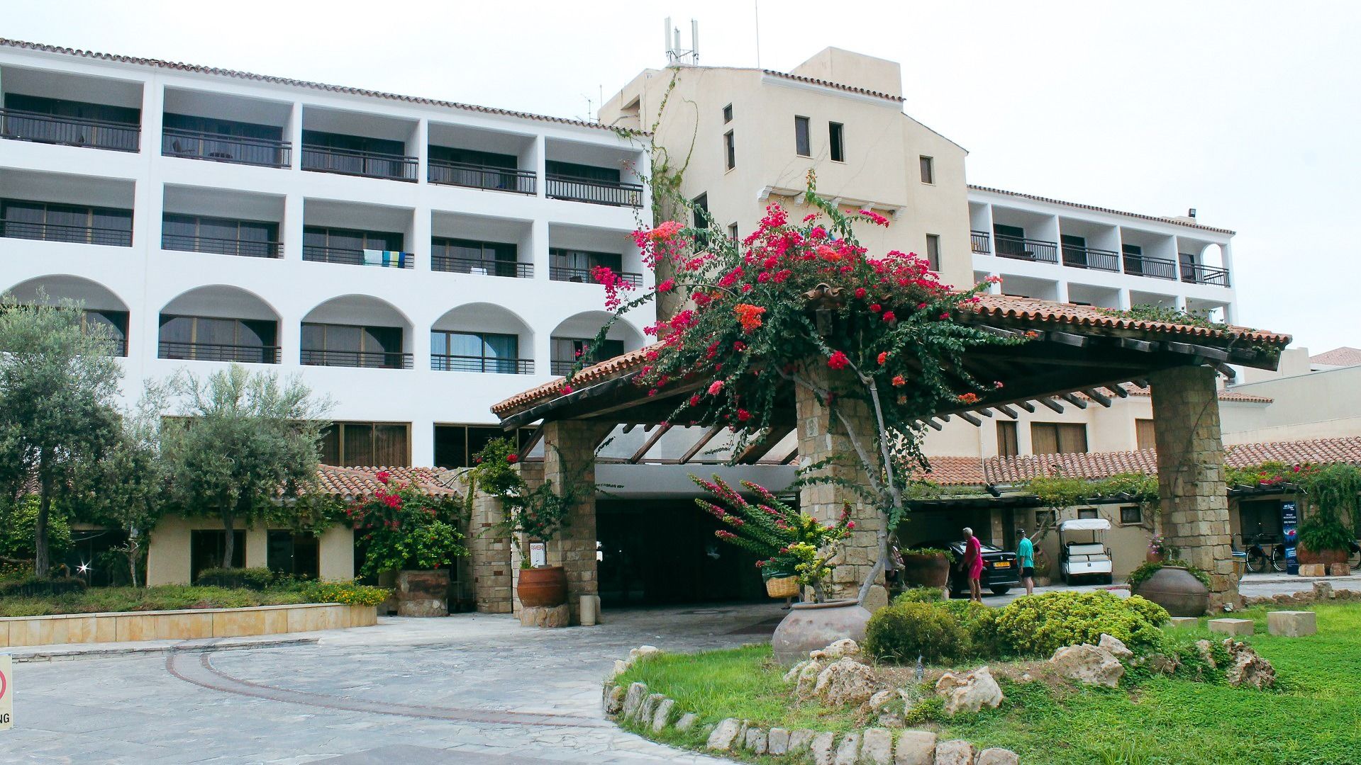 Eleganter Eingangsbereich des Coral Beach Hotel & Resort mit blühenden Bougainvillea und mediterranem Flair.