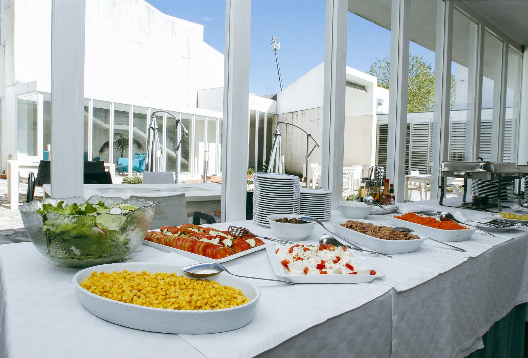 Buffettisch mit Salaten, frischem Gemüse und großer Fensterfront mit Blick auf einen Innenhof.