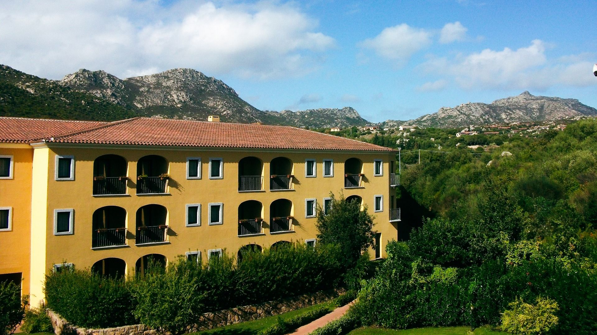 Außenansicht des Geovillage Resorts mit gelber Fassade, Balkonen und Blick auf eine grüne Hügellandschaft.