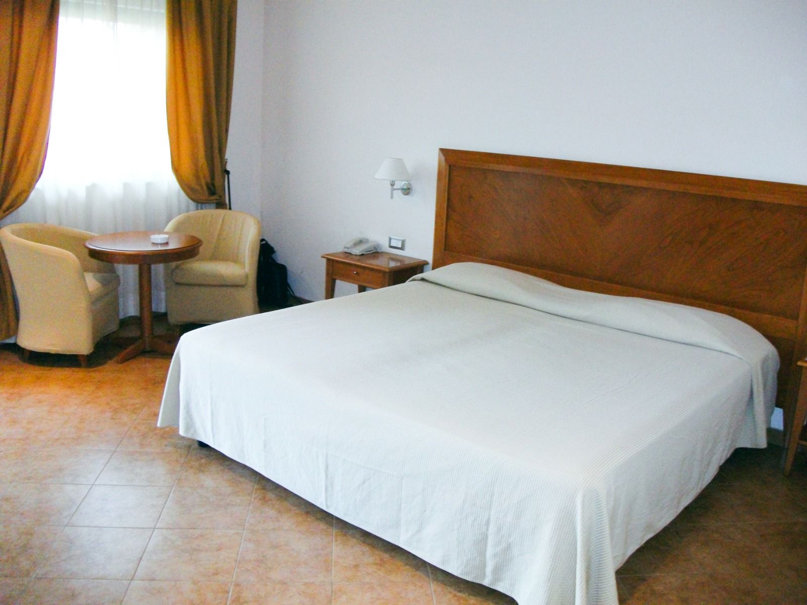 Helles Doppelzimmer mit großem Bett, gemütlicher Sitzecke und goldenen Vorhängen