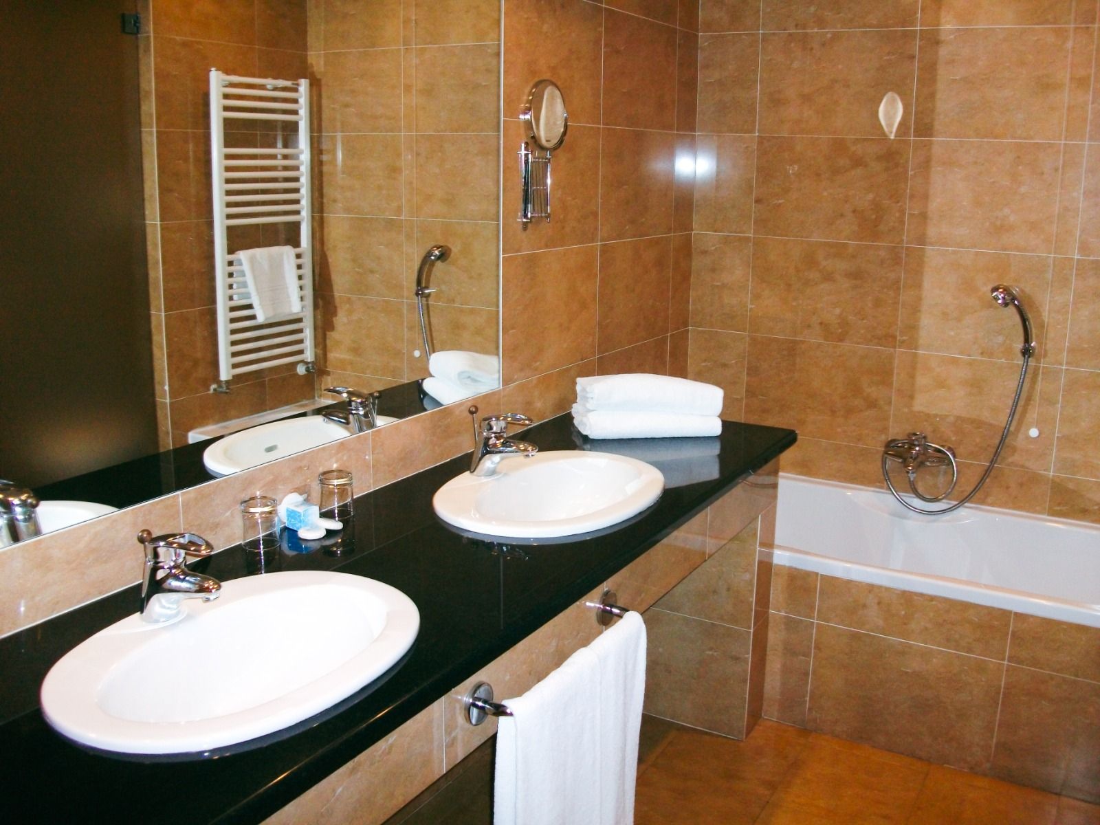 Badezimmer mit zwei Waschbecken, einer Badewanne und modernen Fliesen in warmen Brauntönen