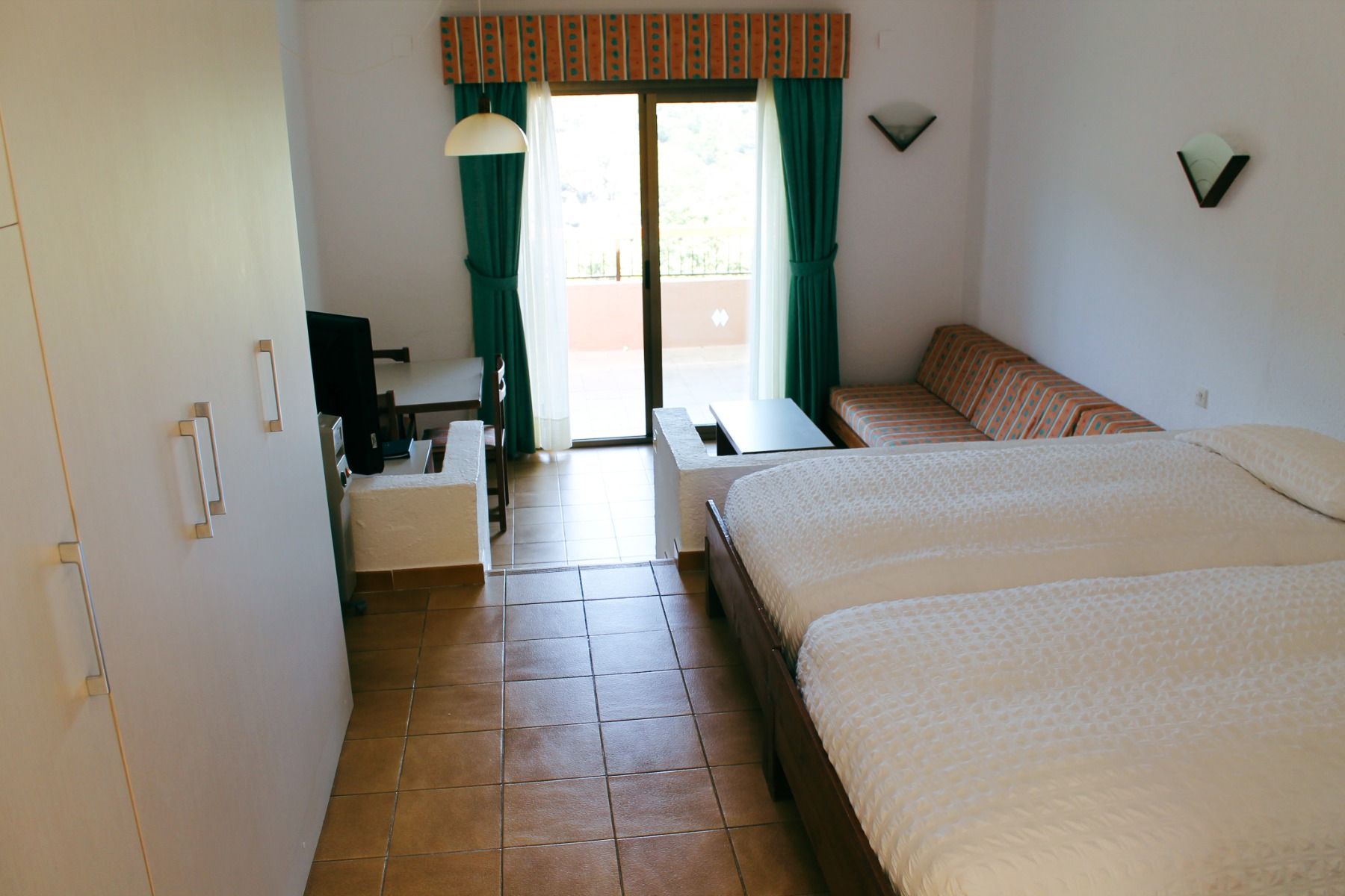 Geräumiges Hotelzimmer mit Doppelbett, Balkonzugang und gemütlichem Sofa.