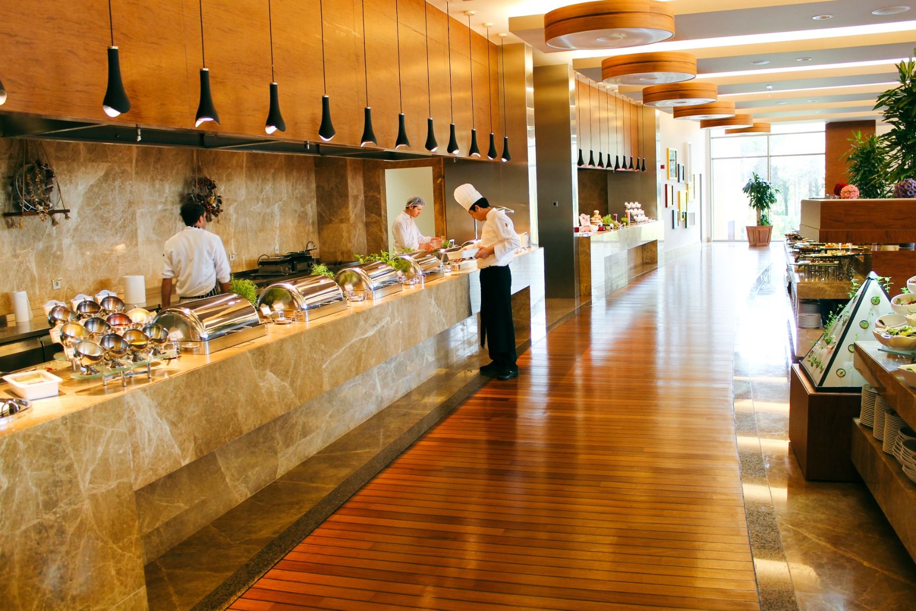 Elegantes Restaurant mit Holzdekor, Buffetbereich und Chefköchen, die frische Gerichte zubereiten.