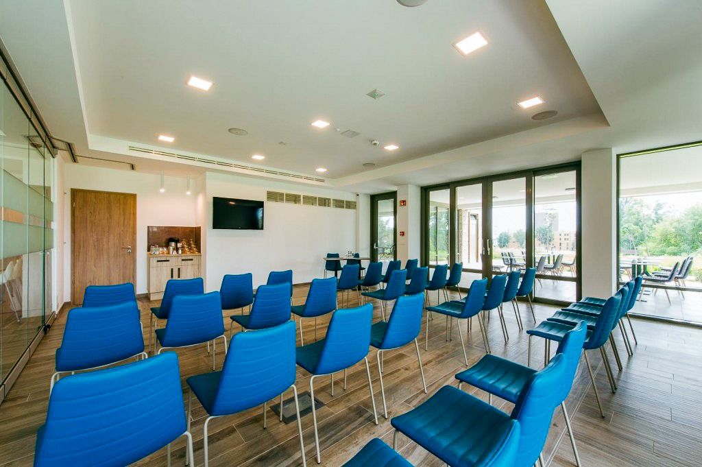 Moderner Konferenzraum mit blauen Stühlen, Holzboden und Glaswänden, die Tageslicht hereinlassen. Perfekt für Meetings und Veranstaltungen.