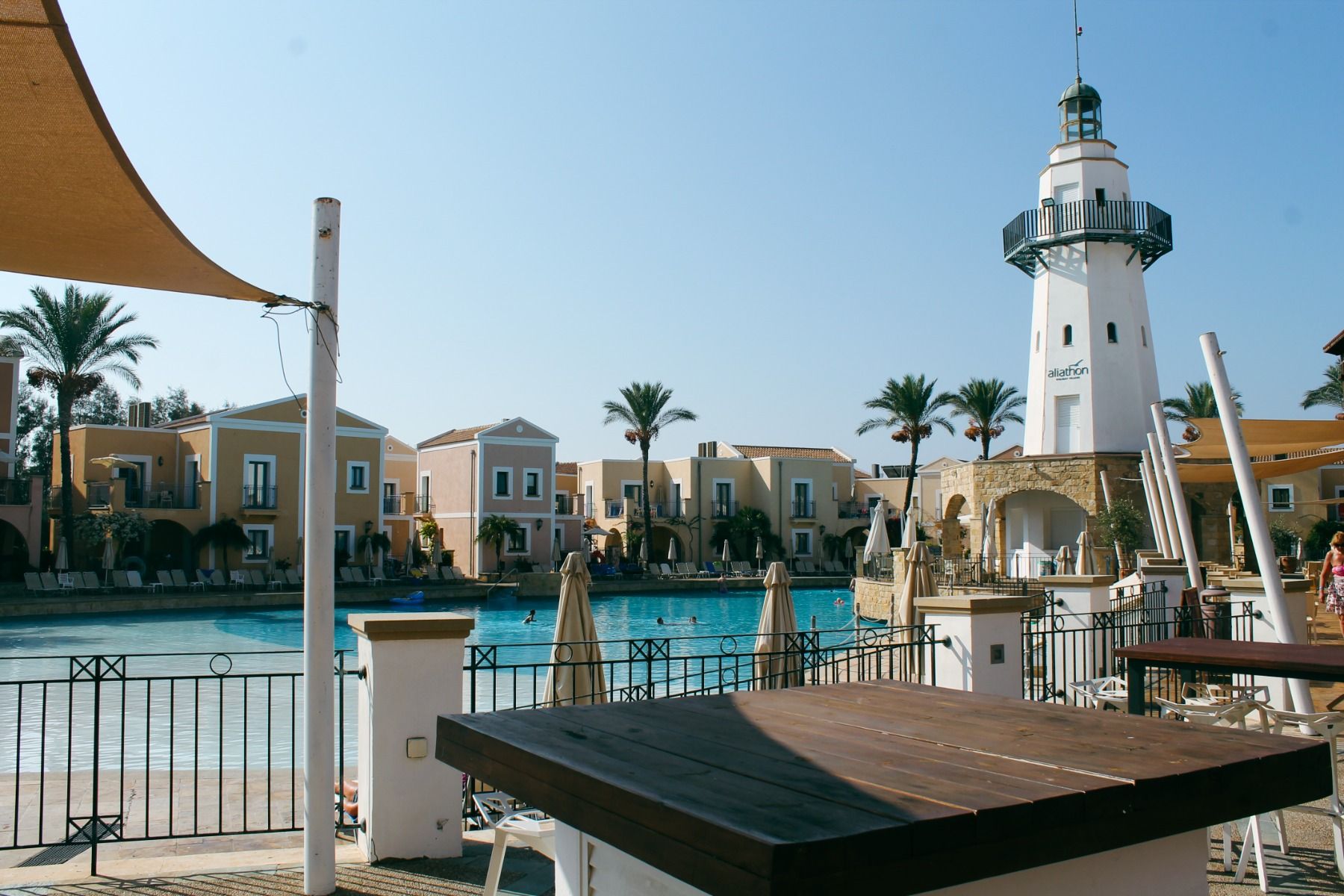 Blick auf den zentralen Leuchtturm und farbenfrohe Gebäude des Aliathon Village, mit Pool und Sonnenterrasse.