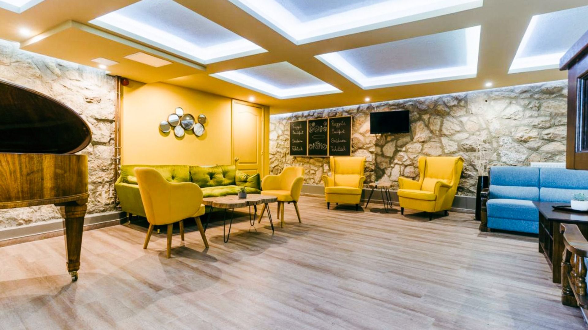 Stilvoll eingerichteter Loungebereich im Hotel Amstel Hattyu Fogado mit gemütlichen Sesseln, einem Klavier und dekorativer Steinwand