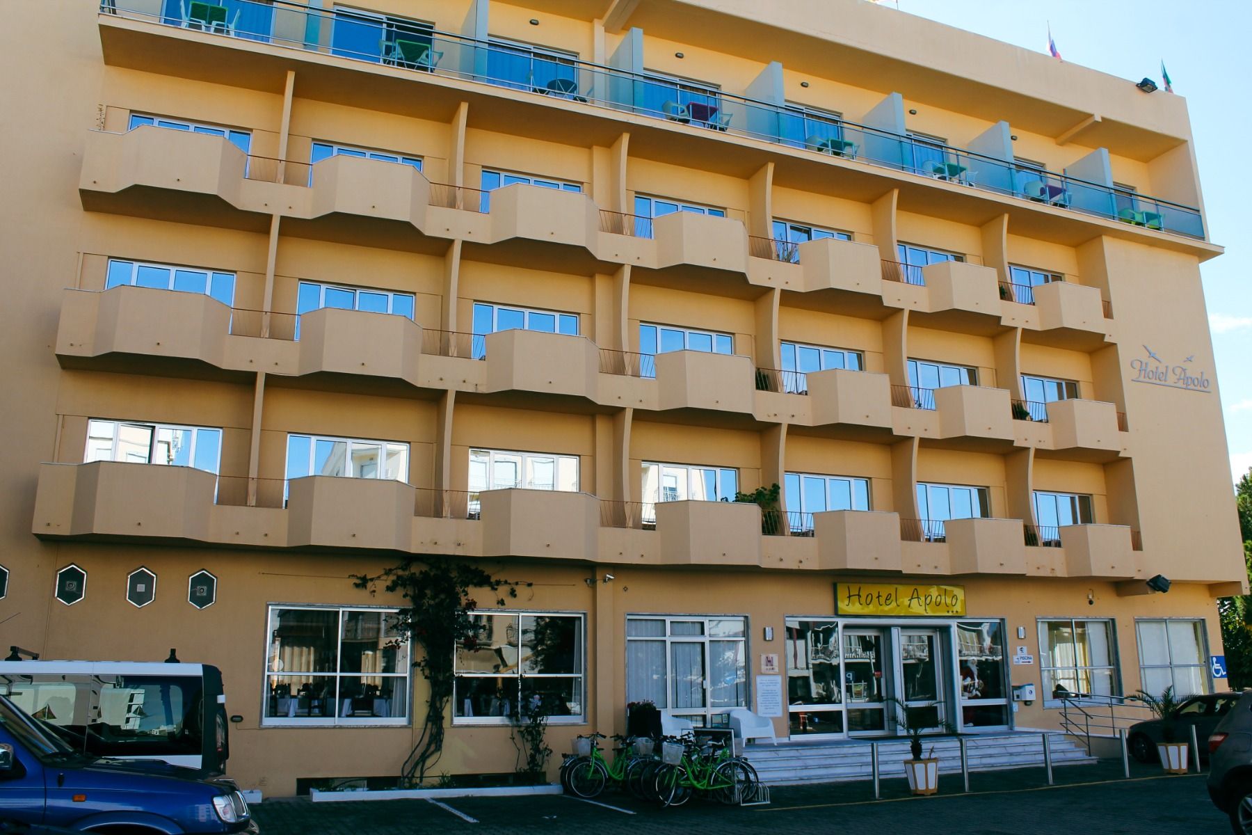 Außenansicht des Hotels Apolo mit gelber Fassade, Balkonen und Fenstern.