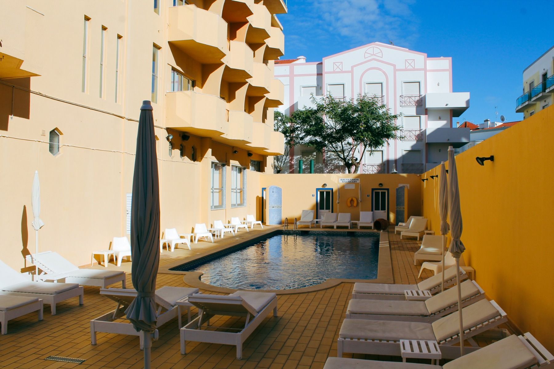 Poolbereich im Innenhof des Hotels Apolo, umgeben von gelber Fassade und Liegestühlen.