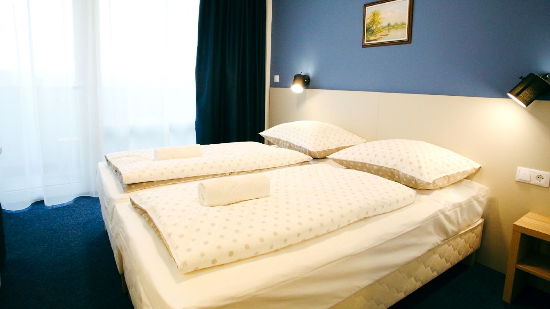 Helles und modernes Zimmer mit einem komfortablen Doppelbett, blauen Wänden und Balkon mit weißen und dunkelblauen Vorhängen.