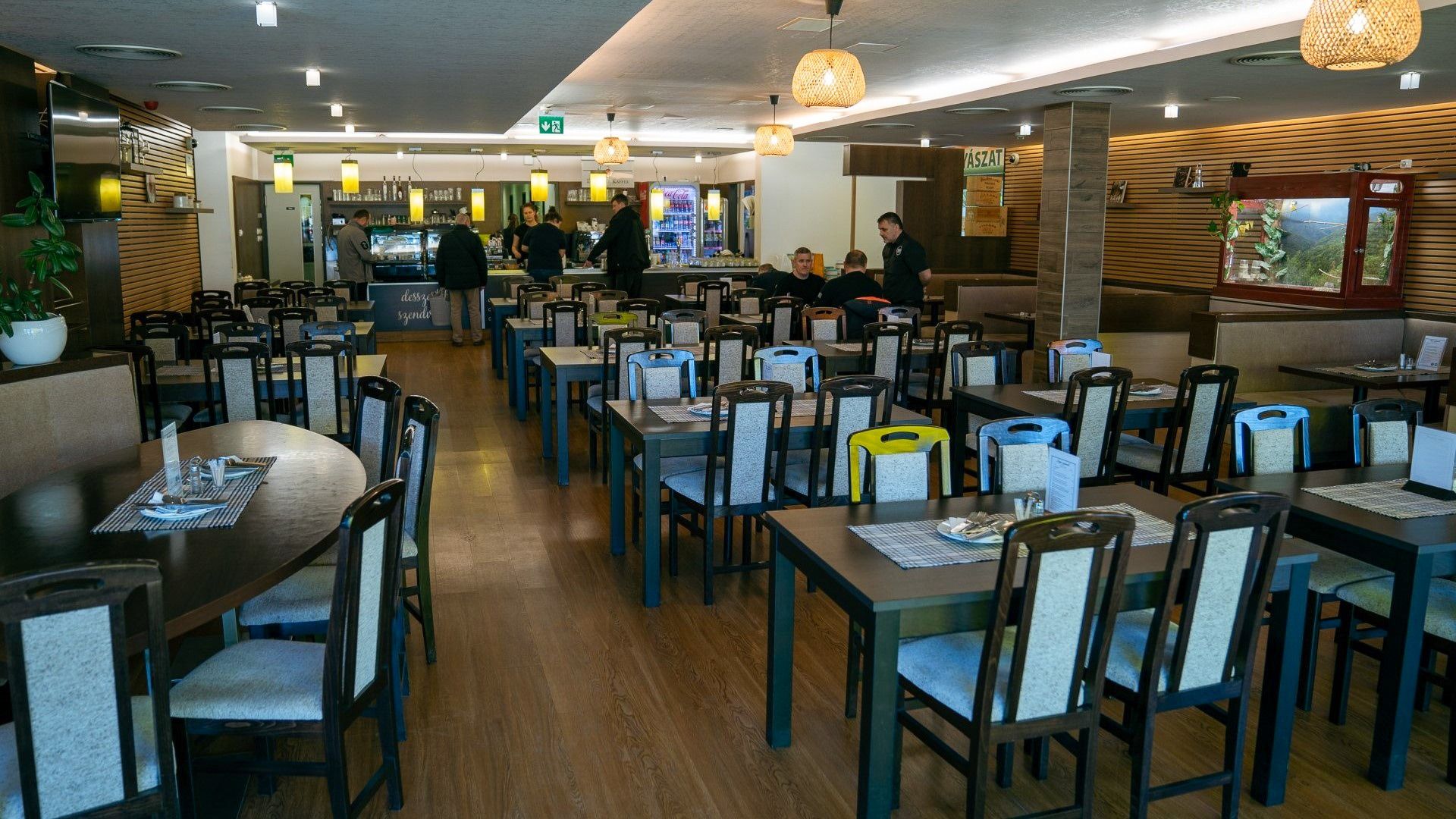 Großes Restaurant mit dunklen Holztischen und gepolsterten Stühlen, gemütliche Atmosphäre mit moderner Beleuchtung und dekorativen Elementen.