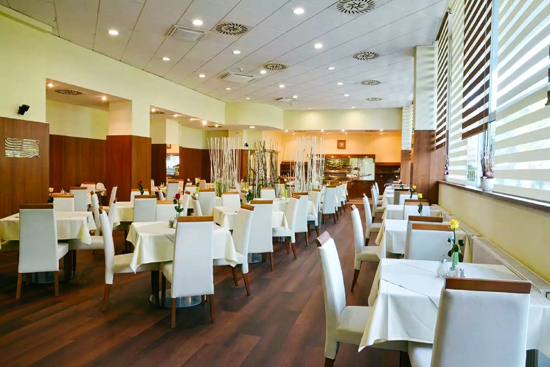 Ein helles, elegantes Restaurant mit weiß gedeckten Tischen, moderner Dekoration und großen Fenstern, die natürliches Licht hereinlassen.