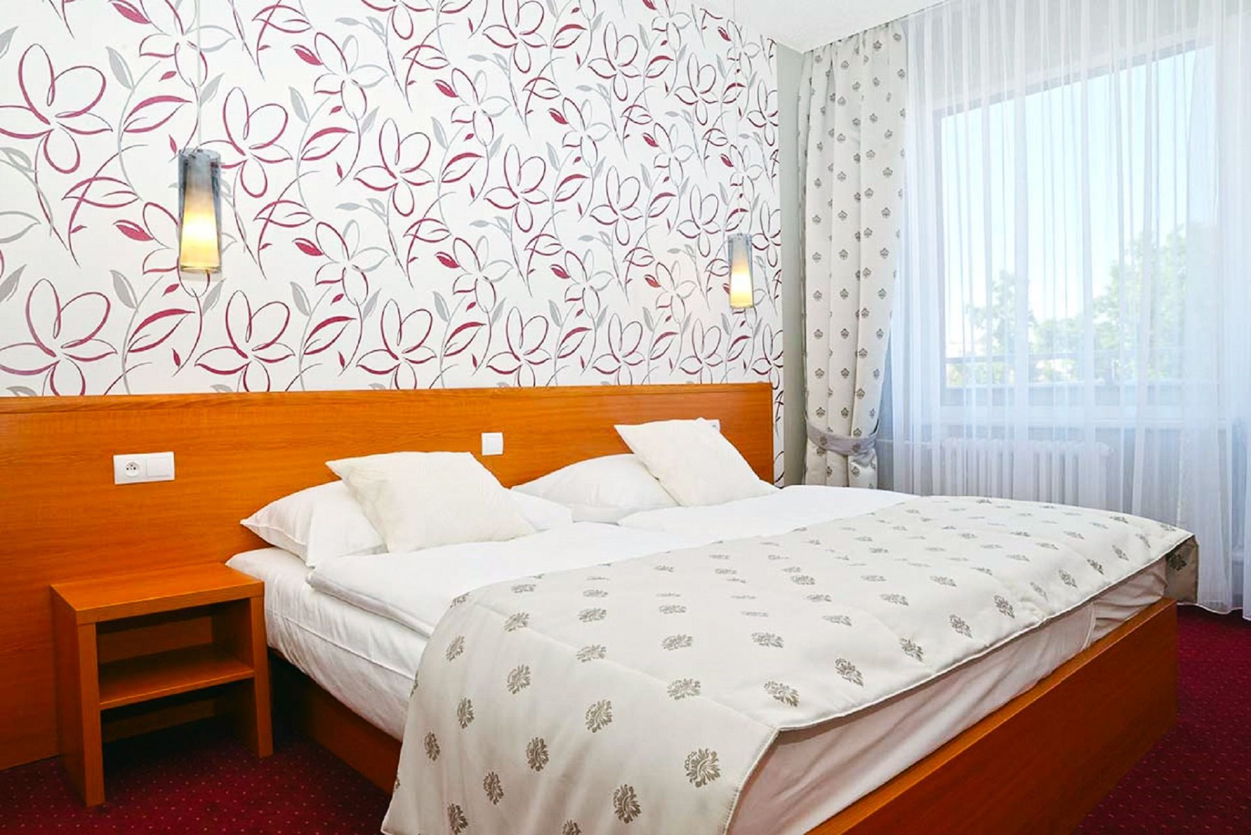 Ein stilvolles Zimmer mit einem großen Doppelbett, floral gemusterten Tapeten, eleganten Vorhängen und modernem Dekor.